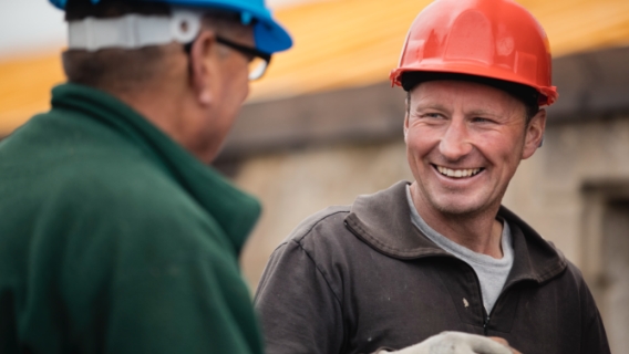 Two roofers wearing hard hats smile and laugh