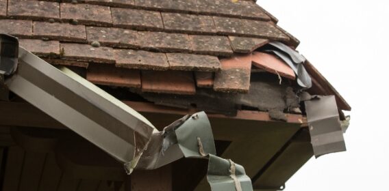 An image of damaged shingles and gutters on the corner of a roof.