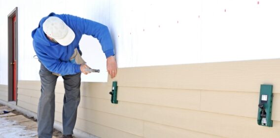 A man wearing a blue shirt and white hat from Saint Louis Residential Roofing secures siding on a home.